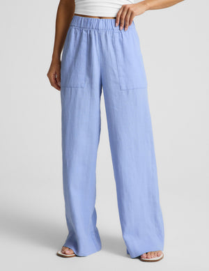 Woman wearing a white strapless top and blue linen pants against a plain background. 