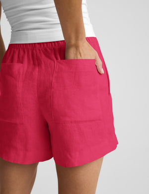 Woman wearing a white halter tank top and red linen shorts against a plain background. 