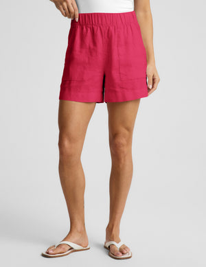 Woman wearing a white halter tank top and red linen shorts against a plain background. 