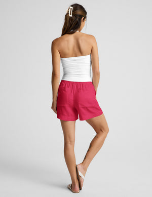Woman wearing a white halter tank top and red linen shorts against a plain background. 