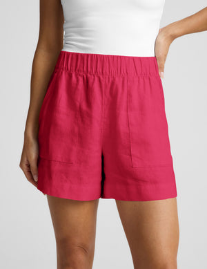 Woman wearing a white halter tank top and red linen shorts against a plain background. 