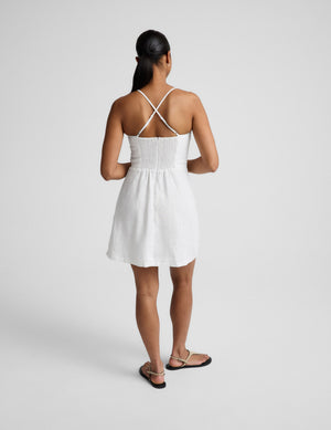 Woman wearing a white mini linen dress against a plain background. 