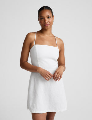 Woman wearing a white mini linen dress against a plain background. 