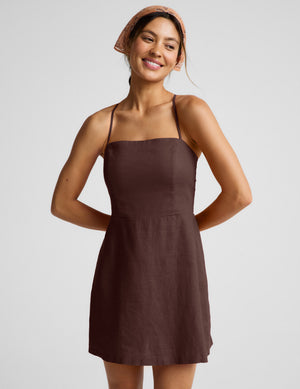 Woman wearing a brown mini linen dress against a plain background. 