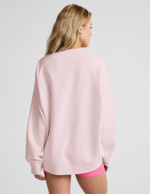 Woman wearing a pink oversized sweatshirt and pink biker shorts against a plain background. 