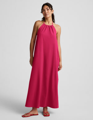 Woman wearing a red halter maxi dress with an open back against a light gray background. 