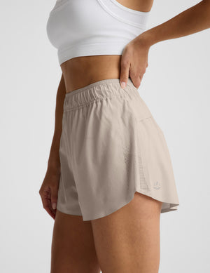 Woman wearing a white sports bra and beige shorts on a plain background. 