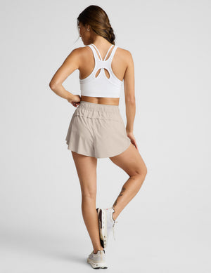 Woman wearing a white sports bra and beige shorts on a plain background. 