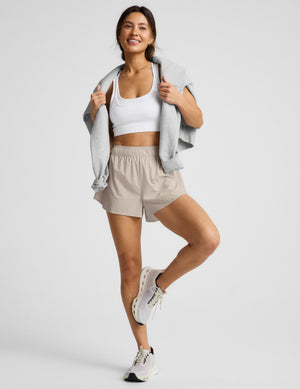 Woman wearing a white sports bra and beige shorts on a plain background. 