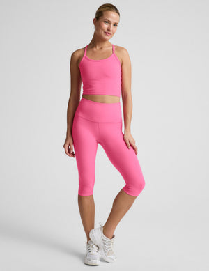 Woman wearing a pink cropped tank top and pink pedal pusher leggings against a plain background. 