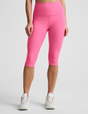 Woman wearing a pink cropped tank top and pink pedal pusher leggings against a plain background. 