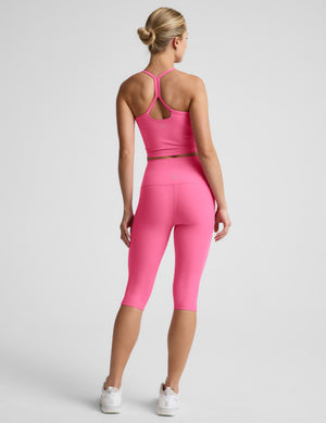 Woman wearing a pink cropped tank top and pink pedal pusher leggings against a plain background. 