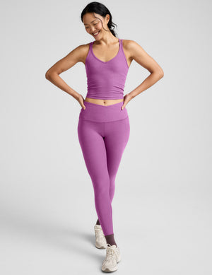 Woman wearing a purple tank top and leggings against a plain background. 
