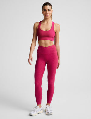 Woman wearing a red bra and leggings against a light gray background. 