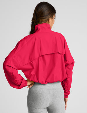 Woman wearing a bright red jacket and gray shorts on a light gray background. 