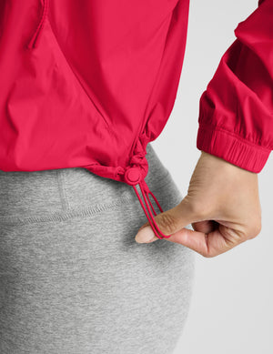 Woman wearing a bright red jacket and gray shorts on a light gray background. 