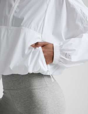 Woman wearing a white half-zip jacket and gray biker shorts against a plain background. 