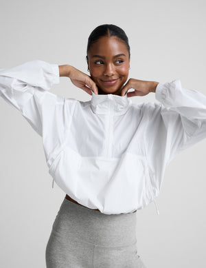 Woman wearing a white half-zip jacket and gray biker shorts against a plain background. 
