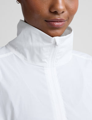 Woman wearing a white half-zip jacket and gray biker shorts against a plain background. 