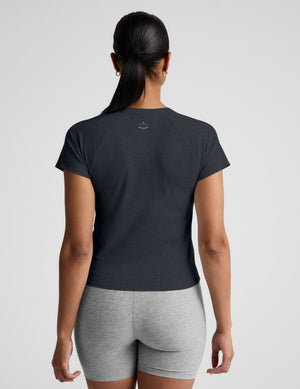 Woman wearing a navy blue active short sleeve top and gray biker shorts against a plain background. 