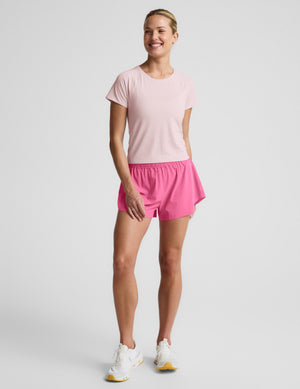 Woman wearing a light pink active short sleeve top and pink running shorts against a plain background. 