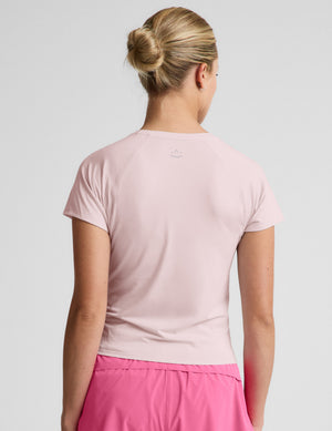 Woman wearing a light pink active short sleeve top and pink running shorts against a plain background. 