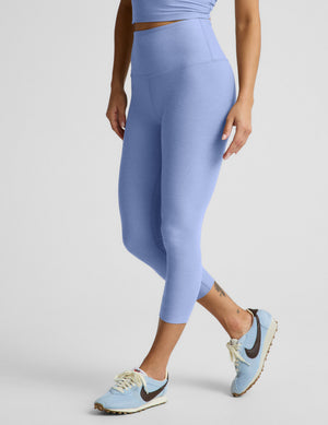 Woman wearing a blue cropped tank top and capri leggings against a plain background. 