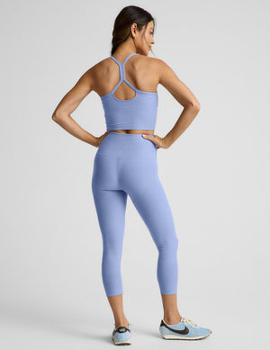 Woman wearing a blue cropped tank top and capri leggings against a plain background. 