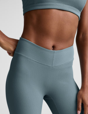 Woman wearing a blue ribbed bra and blue ribbed pedal pushers against a plain background. 