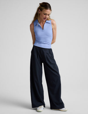 Woman wearing a light blue sleeveless polo shirt and black pants on a plain background. 