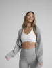 Woman in a grey cropped shrug, white bra, and grey pedal pusher style leggings. 