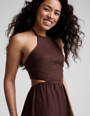 Woman wearing a brown halter neck midi dress on a plain background. 