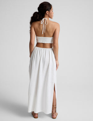 Woman wearing a white midi length halter dress against a plain background. 