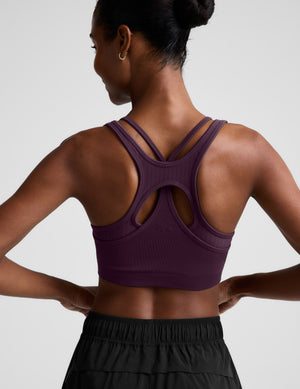 Woman wearing a purple sports bra and black shorts on a plain background. 
