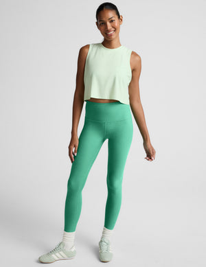 Woman wearing a light green sleeveless top and leggings against a plain background. 