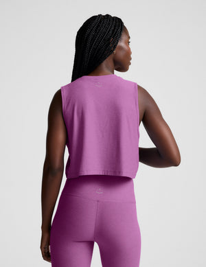 Woman wearing a purple cropped tank and leggings against a plain background. 