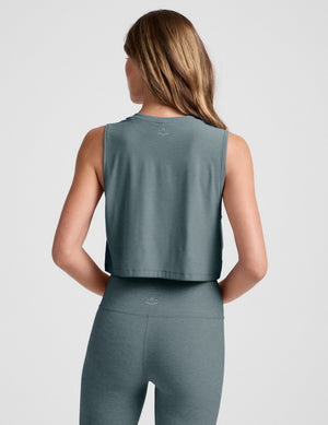 Woman wearing a gray sleeveless top and leggings on a light gray background. 
