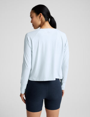Woman wearing a light blue long sleeve and navy blue biker shorts against a plain background. 