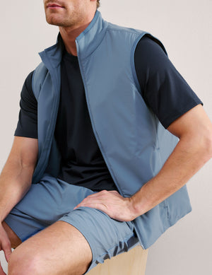 Man wearing a light blue vest over a black shirt on a plain background. 