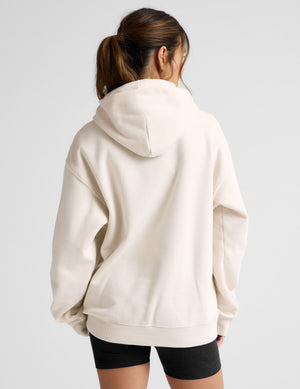 Woman wearing a white oversized hoodie and black shorts on a light gray background. 