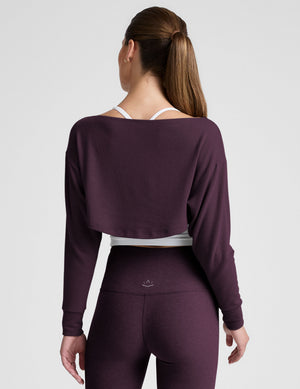 model wearing a white cropped tank and purple leggings with a purple shrug on a light background. 