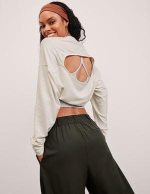 model wearing a white long-sleeve shrug with cut-out design and green pants on a light gray background. 