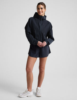 Woman wearing a blue hooded jacket and shorts against a plain background. 