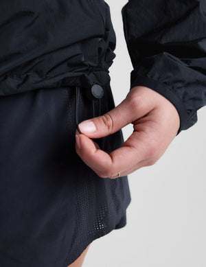 Woman wearing a blue hooded jacket and shorts against a plain background. 