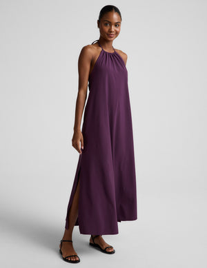 Woman wearing a purple halter neck maxi dress on a plain background. 