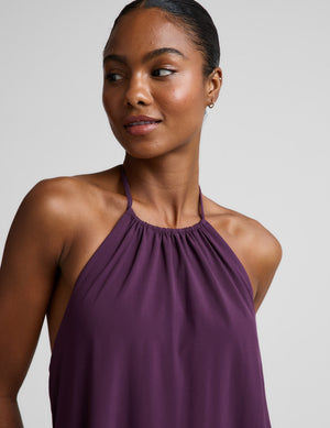 Woman wearing a purple halter neck maxi dress on a plain background. 