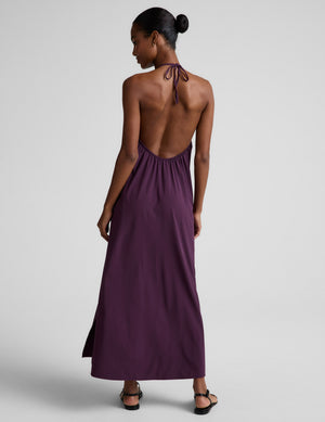 Woman wearing a purple halter neck maxi dress on a plain background. 
