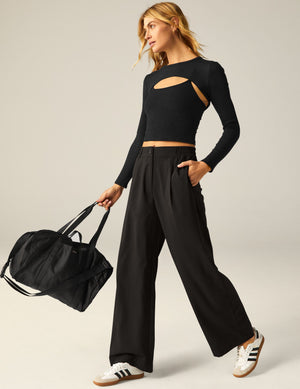 Black Status Wide Leg Trousers on a walking model, featuring front pleats, a zip fly, and a relaxed, flowy silhouette.