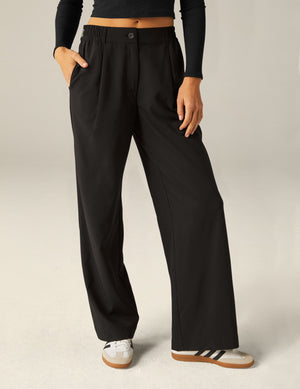 Front view of black Status Wide Leg Trousers with a pleated front and elastic waistband on a model with hand in pocket.