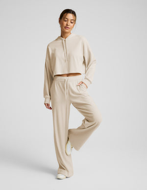 Woman wearing a beige cropped hoodie and pants on a light gray background. 